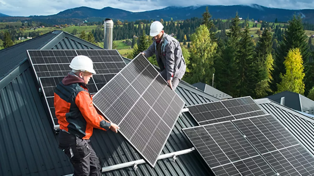 Two workers are installing solar panels on the roof of a house.