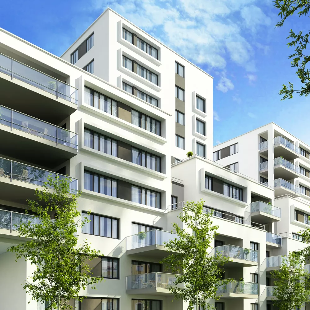 Modern white apartment buildings with multiple balconies, large windows, and surrounding green trees under a clear blue sky.