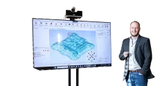 Man standing beside a screen displaying 3D terrain modeling software.